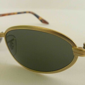 May include: Gold-tone oval sunglasses with tortoise shell arms. The lenses are dark green.