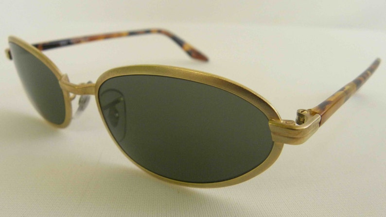 May include: Gold-tone oval sunglasses with tortoise shell arms. The lenses are dark green.