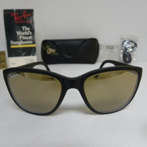 May include: Black Ray-Ban sunglasses with brown mirrored lenses. The sunglasses are in a case with a Ray-Ban logo. The World's Finest Sunglasses text is on a tag.