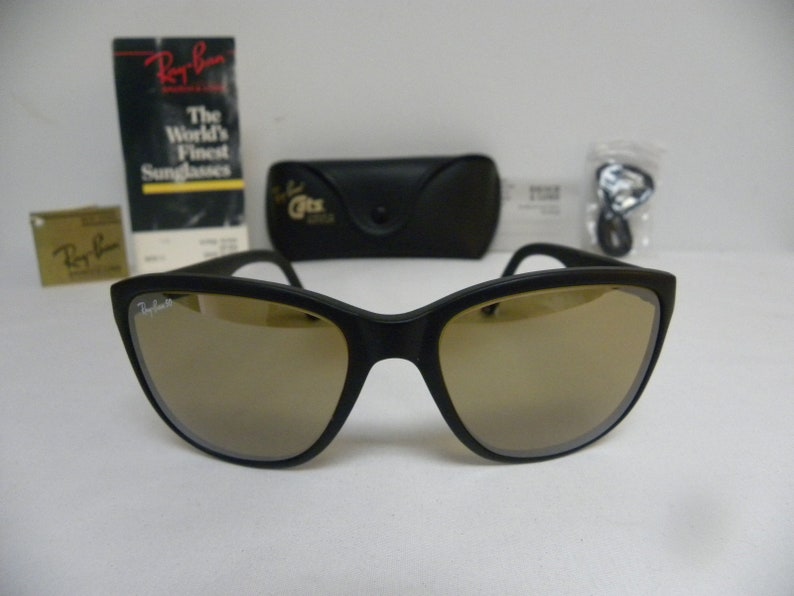 May include: Black Ray-Ban sunglasses with brown mirrored lenses. The sunglasses are in a case with a Ray-Ban logo. The World's Finest Sunglasses text is on a tag.