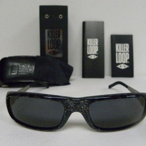May include: Black sunglasses with a speckled pattern on the frame. The sunglasses are in a case with the words "Killer Loop" printed on it.