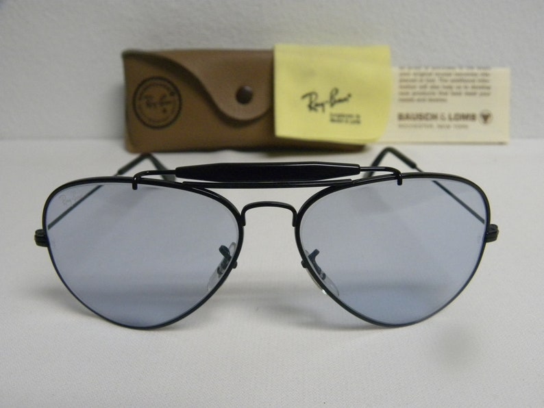 May include: Black aviator sunglasses with a metal frame and blue tinted lenses. The sunglasses have a black nose bridge and a black metal bar across the top of the frame.