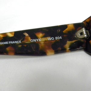 K&ouml;nnte beinhalten: Nahaufnahme einer Sonnenbrillenfassung aus Schildpattmuster mit dem Text "FRAME FRANCE ONYX WO 804", der auf der Innenseite der Fassung aufgedruckt ist.