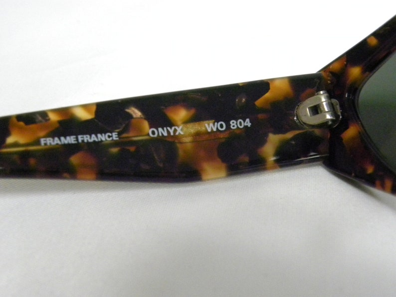 K&ouml;nnte beinhalten: Nahaufnahme einer Sonnenbrillenfassung aus Schildpattmuster mit dem Text "FRAME FRANCE ONYX WO 804", der auf der Innenseite der Fassung aufgedruckt ist.
