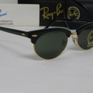 Puede incluir: Gafas de sol Ray-Ban negras con lentes verdes y detalles dorados. Las gafas tienen un estilo aviador cl&aacute;sico con un fino marco de metal.