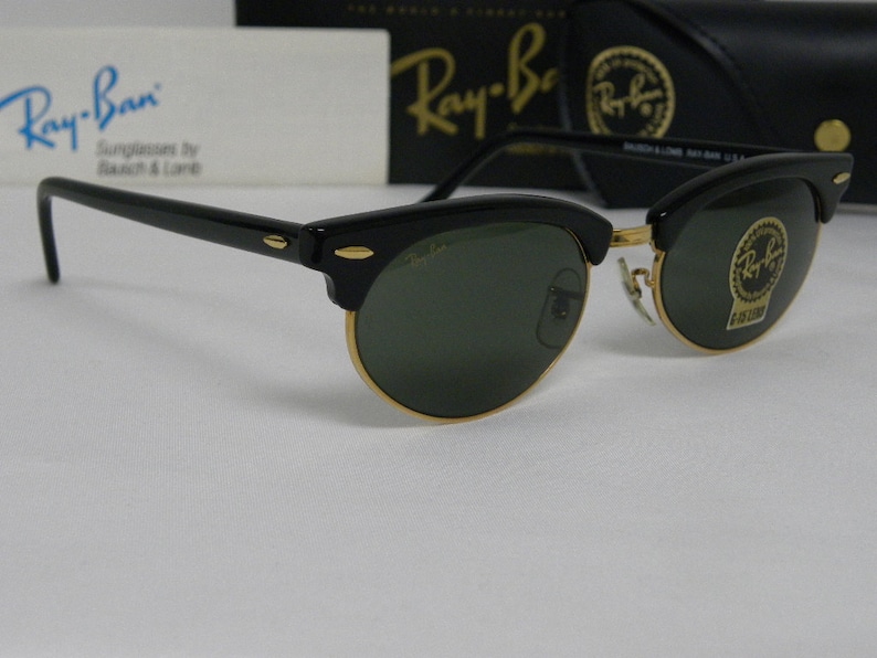 Puede incluir: Gafas de sol Ray-Ban negras con lentes verdes y detalles dorados. Las gafas tienen un estilo aviador cl&aacute;sico con un fino marco de metal.