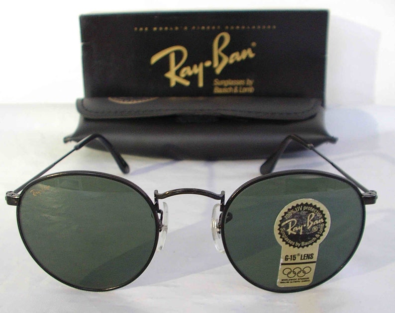 K&ouml;nnte beinhalten: Schwarze Ray-Ban Sonnenbrille mit gr&uuml;nen Gl&auml;sern. Die Sonnenbrille hat einen runden Rahmen und eine Metallkonstruktion. Die Gl&auml;ser sind mit "G-15" gekennzeichnet und haben einen UV-Schutzaufkleber.