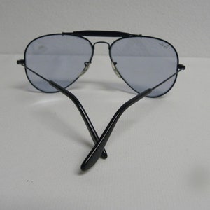 May include: Black aviator sunglasses with blue tinted lenses. The sunglasses are folded in half with the arms crossed.