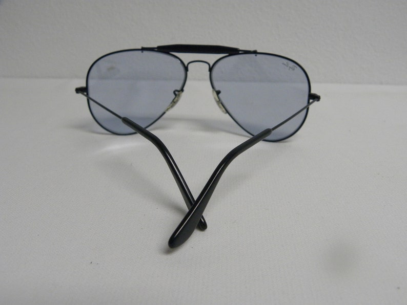 May include: Black aviator sunglasses with blue tinted lenses. The sunglasses are folded in half with the arms crossed.