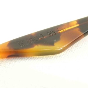 May include: Close-up of a brown tortoise shell plastic temple tip with the text "W2853 NY AS" embossed on it.