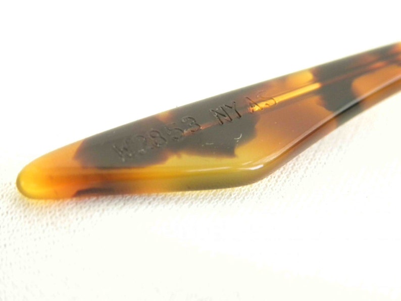 May include: Close-up of a brown tortoise shell plastic temple tip with the text "W2853 NY AS" embossed on it.