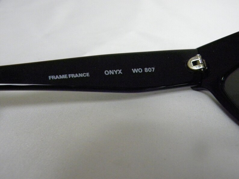 Puede incluir: Primer plano del marco negro de unas gafas de sol. El marco tiene el texto "FRAME FRANCE ONYX WO 807" impreso en &eacute;l.