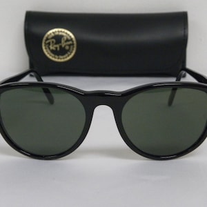 Puede incluir: Gafas de sol redondas negras con lentes verdes. Las gafas de sol est&aacute;n en una caja negra con el logotipo de Ray-Ban.