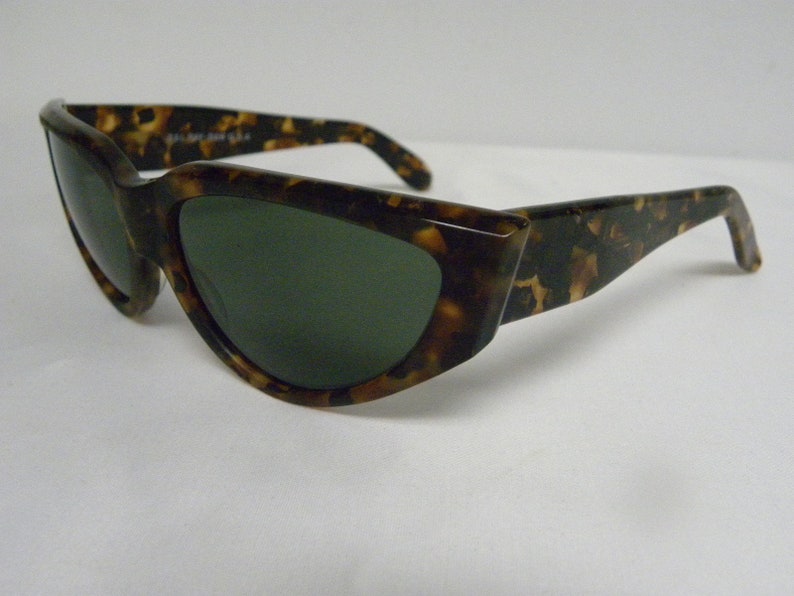 K&ouml;nnte beinhalten: Schildkr&ouml;ten-Sonnenbrille mit dunkelgr&uuml;nen Gl&auml;sern. Die Sonnenbrille hat eine einzigartige, eckige Form.