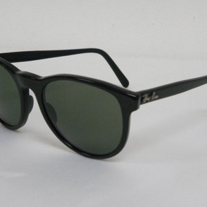 Puede incluir: Gafas de sol de pl&aacute;stico negro con lentes verdes y el logotipo de Ray-Ban en el lateral.