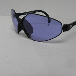 May include: Black sunglasses with a unique, angular frame and purple lenses. The sunglasses have a flexible, adjustable arm.