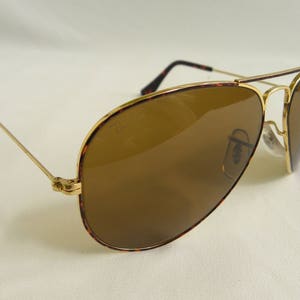 K&ouml;nnte beinhalten: Goldene Aviator-Sonnenbrille mit braunen Gl&auml;sern. Der Rahmen hat ein Schildpattmuster.