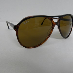 Puede incluir: Gafas de sol aviador de carey con lentes marrones. Las gafas tienen una barra de metal sobre el puente de la nariz y el logotipo de Ray-Ban es visible en la lente derecha.