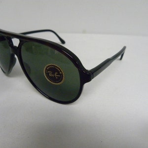 May include: Black aviator sunglasses with green lenses and a Ray-Ban logo on the right lens.