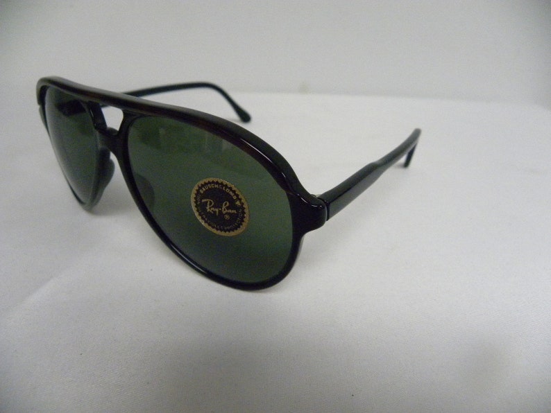 May include: Black aviator sunglasses with green lenses and a Ray-Ban logo on the right lens.