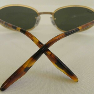 May include: A pair of gold-rimmed sunglasses with tortoiseshell arms. The lenses are green and oval-shaped.