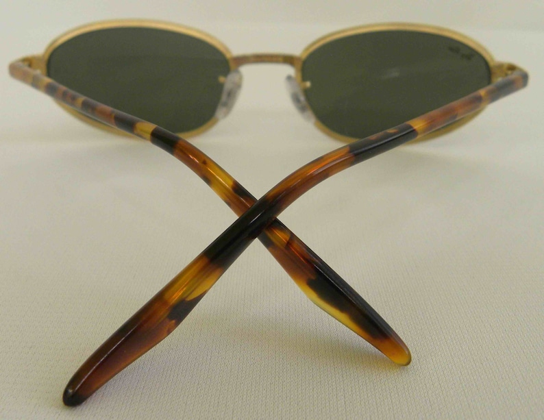 May include: A pair of gold-rimmed sunglasses with tortoiseshell arms. The lenses are green and oval-shaped.