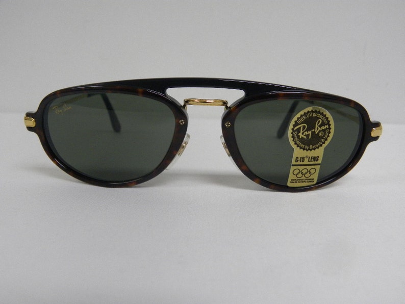 May include: Ray-Ban sunglasses with a tortoiseshell frame and dark green lenses. The sunglasses have gold accents on the temples and bridge. The lenses have a sticker that reads "Ray-Ban G-15 Lens".