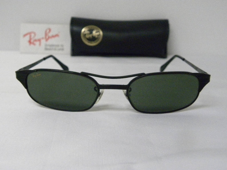 Puede incluir: Gafas de sol negras con montura de metal y lentes verde oscuro. Las gafas de sol est&aacute;n sobre una superficie blanca.