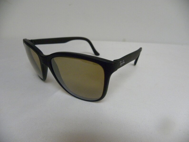 May include: Black plastic sunglasses with brown lenses. The sunglasses have a Ray-Ban logo on the side.