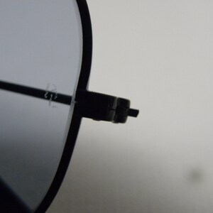 May include: Close-up of the black metal frame of a pair of sunglasses. The frame has a hinge on the right side.