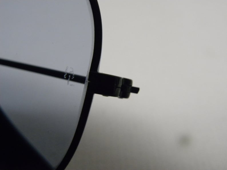 May include: Close-up of the black metal frame of a pair of sunglasses. The frame has a hinge on the right side.