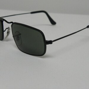 May include: Black square-shaped sunglasses with thin metal frames and dark green lenses.