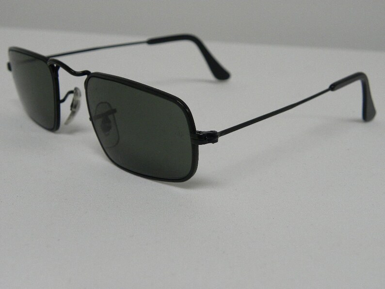 May include: Black square-shaped sunglasses with thin metal frames and dark green lenses.