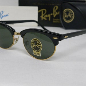 Puede incluir: Gafas de sol Ray-Ban negras con lentes verdes y detalles dorados. Las gafas tienen un estilo aviador cl&aacute;sico con un fino marco de metal y una lente ancha y curvada.