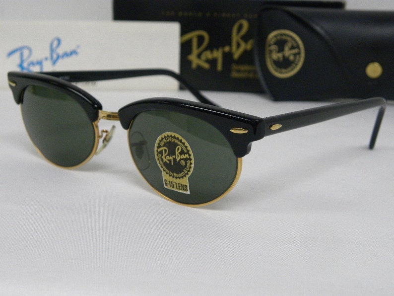 Puede incluir: Gafas de sol Ray-Ban negras con lentes verdes y detalles dorados. Las gafas tienen un estilo aviador cl&aacute;sico con un fino marco de metal y una lente ancha y curvada.