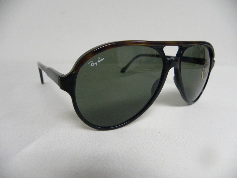 May include: Black and brown aviator sunglasses with green lenses. The sunglasses have a Ray-Ban logo on the right lens.