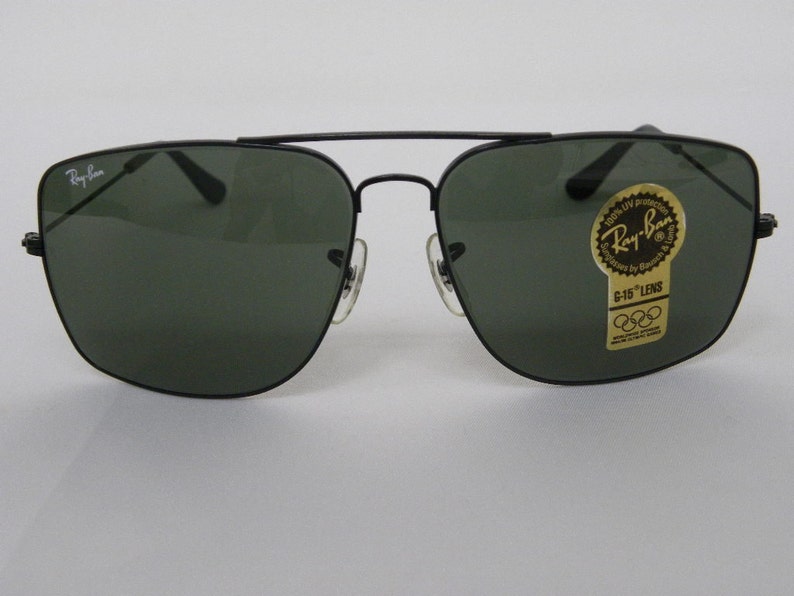 May include: Black Ray-Ban sunglasses with green lenses. The sunglasses have a square frame and a gold sticker on the right lens that says "Ray-Ban" and "G-15 Lens".