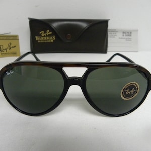May include: A pair of Ray-Ban sunglasses with tortoise shell frames and green lenses. The sunglasses have a Ray-Ban logo on the left lens and a Ray-Ban sticker on the right lens.