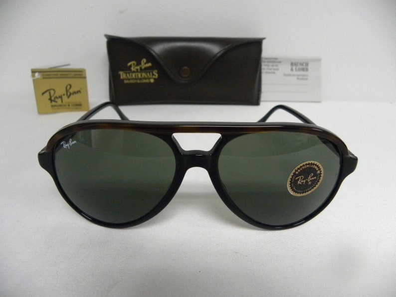 May include: A pair of Ray-Ban sunglasses with tortoise shell frames and green lenses. The sunglasses have a Ray-Ban logo on the left lens and a Ray-Ban sticker on the right lens.
