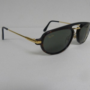 May include: Aviator-style sunglasses with a tortoiseshell frame and green lenses. The sunglasses feature gold-colored arms and the Ray-Ban logo. The lenses are slightly tinted, and the overall design is classic and stylish.