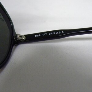 May include: Close-up of the black arm of a pair of sunglasses with the text "B&L RAY-BAN U.S.A." printed in white.