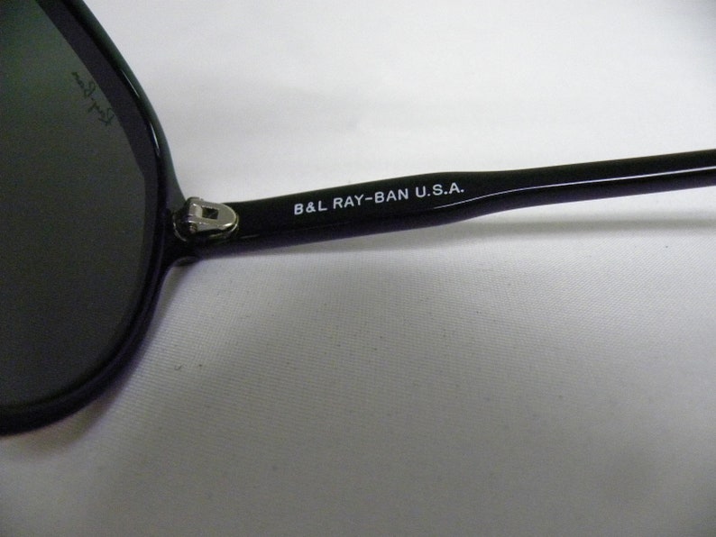 May include: Close-up of the black arm of a pair of sunglasses with the text "B&L RAY-BAN U.S.A." printed in white.