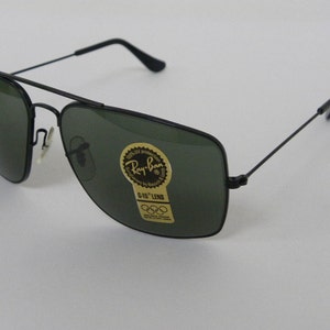 May include: Black Ray-Ban sunglasses with green lenses. The sunglasses have a gold sticker on the right lens that says "Ray-Ban" and "G-15 Lens".