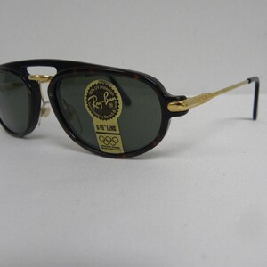 May include: Ray-Ban sunglasses with a dark tortoise shell frame and gold-tone accents. The lenses are dark green, and the sunglasses have a classic aviator shape. A sticker on the lens reads "Ray-Ban G-15 LENS".