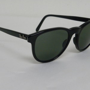 Puede incluir: Gafas de sol Ray-Ban negras con lentes verdes. Las gafas tienen una forma redonda cl&aacute;sica y un dise&ntilde;o sencillo.