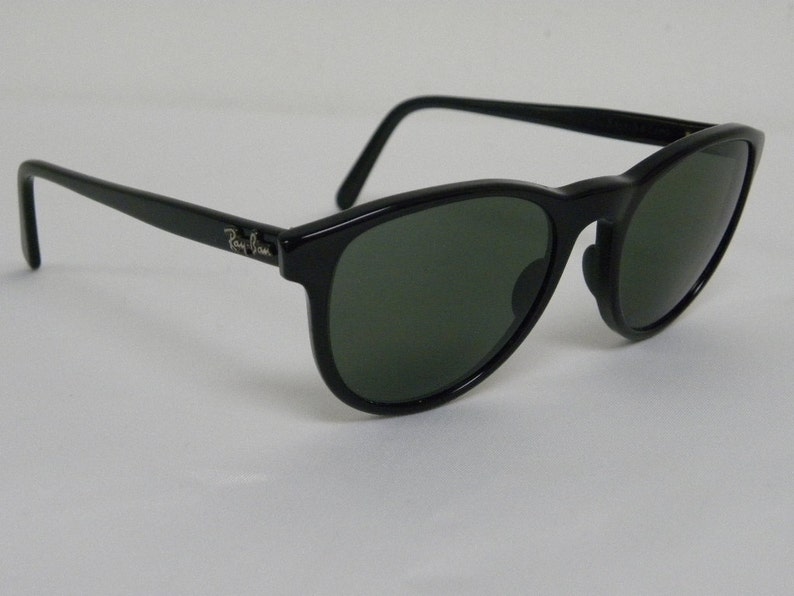 Puede incluir: Gafas de sol Ray-Ban negras con lentes verdes. Las gafas tienen una forma redonda cl&aacute;sica y un dise&ntilde;o sencillo.
