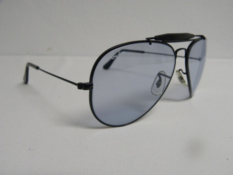 May include: Black aviator sunglasses with a silver nose bridge and Ray-Ban branding on the lens.