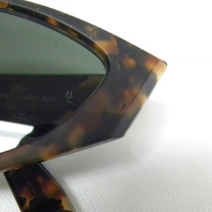 K&ouml;nnte beinhalten: Nahaufnahme einer Sonnenbrille aus Schildpatt mit gr&uuml;nen Gl&auml;sern. Die Sonnenbrille hat eine einzigartige, eckige Form und der Text "Ray-Ban 54 024/3M" ist auf dem Gestell sichtbar.