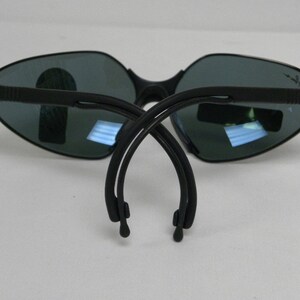 May include: Black Ray-Ban sunglasses with a dark gray lens and a flexible black frame. The sunglasses are folded in half, showing the Ray-Ban logo on both arms.