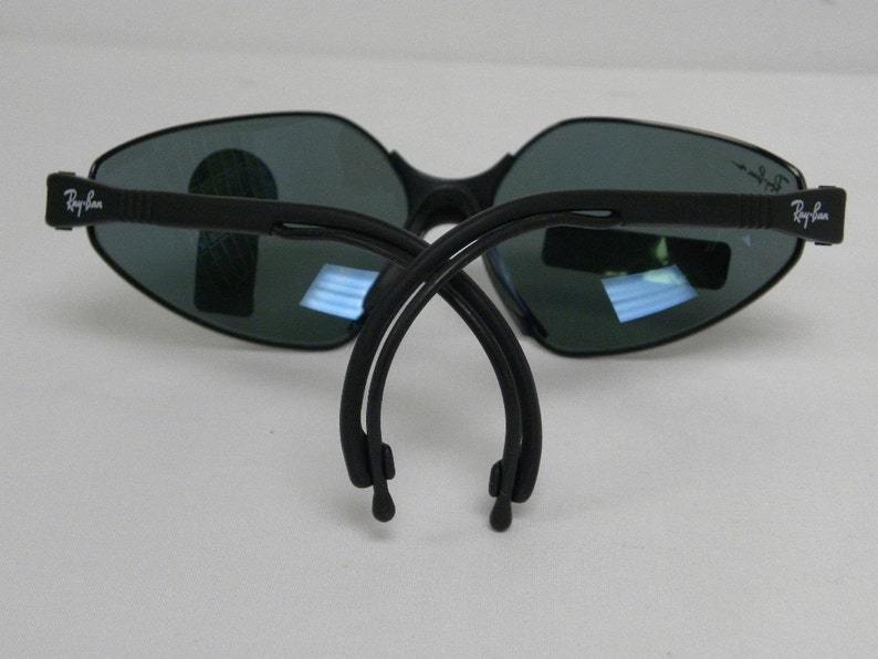 May include: Black Ray-Ban sunglasses with a dark gray lens and a flexible black frame. The sunglasses are folded in half, showing the Ray-Ban logo on both arms.